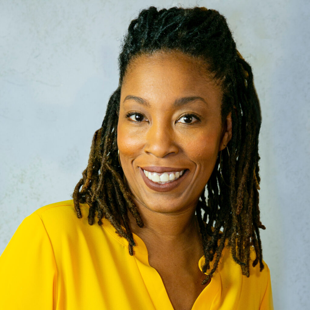 A woman with dreads in yellow shirt smiling.