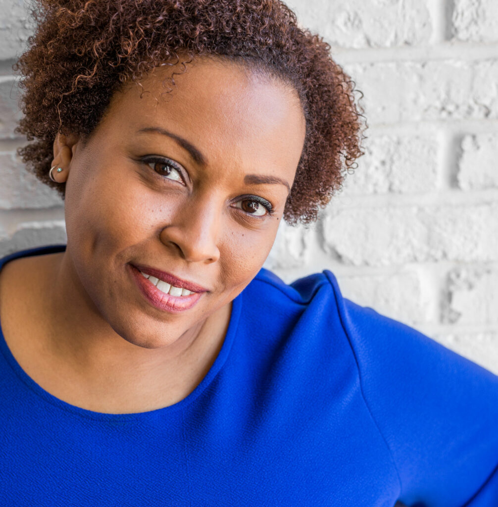 A woman with curly hair wearing blue shirt and smiling.