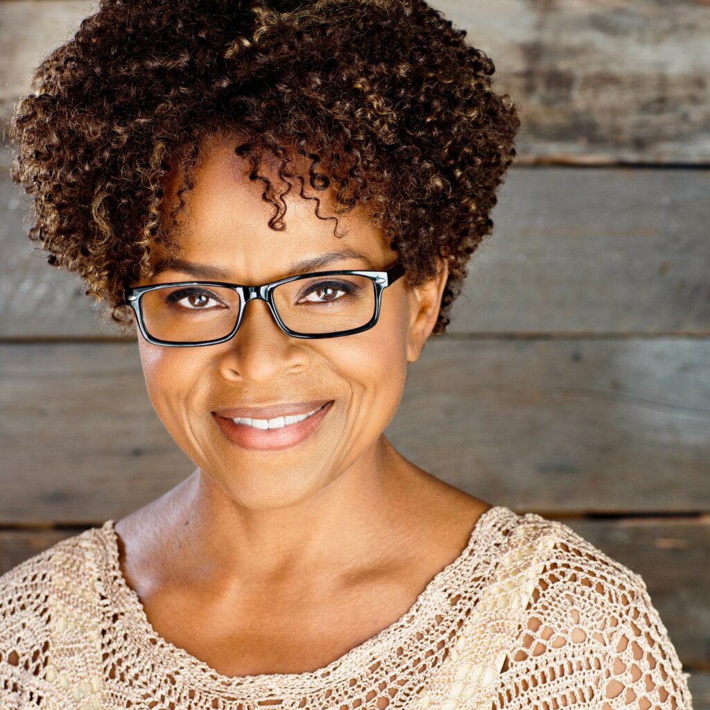 A woman with glasses and curly hair smiling.