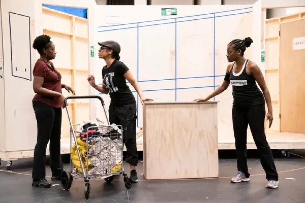 Three women stand around a wooden box and cart.