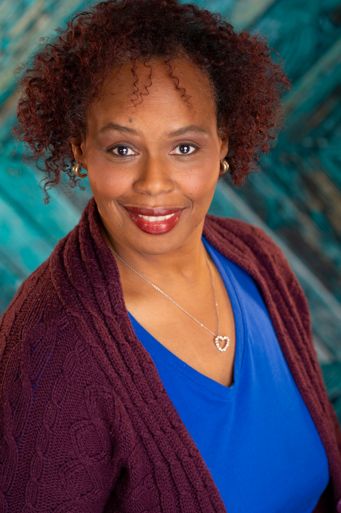 A woman with blue eyes and curly hair wearing a purple shirt.